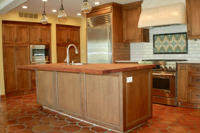 Example of a large arts and crafts single-wall porcelain tile and orange floor eat-in kitchen design in Sacramento with an undermount sink, recessed-panel cabinets, medium tone wood cabinets, marble countertops, white backsplash, brick backsplash, stainless steel appliances and an island