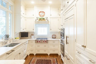 Enclosed kitchen - large traditional u-shaped medium tone wood floor and brown floor enclosed kitchen idea in Little Rock with a double-bowl sink, beaded inset cabinets, white cabinets, quartzite countertops, white backsplash, ceramic backsplash, paneled appliances, a peninsula and beige countertops