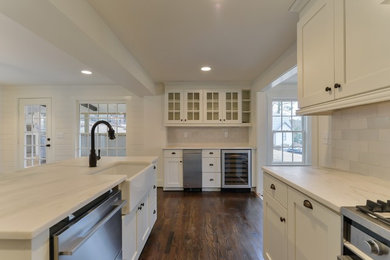 Mid-sized transitional u-shaped dark wood floor eat-in kitchen photo in Birmingham with a farmhouse sink, shaker cabinets, white cabinets, white backsplash, stainless steel appliances, an island, marble countertops and porcelain backsplash