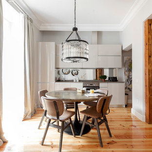 Ejemplo de cocina comedor lineal, actual, de tamaño medio, sin isla, con armarios con paneles lisos, puertas de armario blancas, salpicadero con efecto espejo, electrodomésticos de acero inoxidable, suelo de madera en tonos medios y suelo marrón
