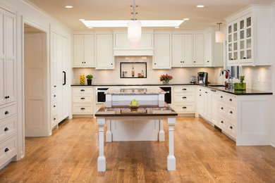 Example of a mid-sized eclectic u-shaped medium tone wood floor kitchen pantry design in Minneapolis with an undermount sink, glass-front cabinets, white cabinets, granite countertops, white backsplash, subway tile backsplash, black appliances and an island