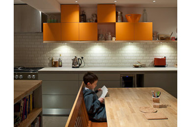 ロンドンにある中くらいなモダンスタイルのおしゃれなキッチン (フラットパネル扉のキャビネット、オレンジのキャビネット、御影石カウンター、黄色いキッチンパネル、セラミックタイルのキッチンパネル、シルバーの調理設備、セラミックタイルの床) の写真