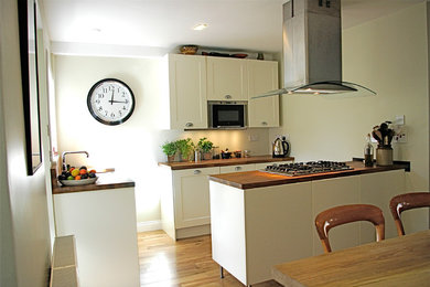 Mid-sized transitional u-shaped light wood floor eat-in kitchen photo in Edinburgh with an undermount sink, shaker cabinets, white cabinets, wood countertops, stainless steel appliances and a peninsula