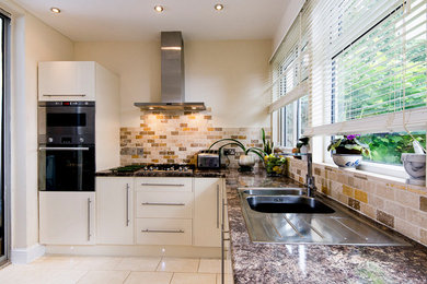 This is an example of a medium sized contemporary u-shaped enclosed kitchen in London with a submerged sink, flat-panel cabinets, beige cabinets, beige splashback, stone tiled splashback, integrated appliances, ceramic flooring, no island and beige floors.
