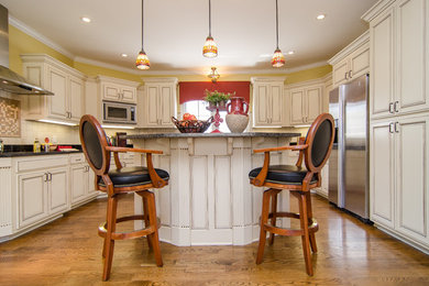Inspiration for a large timeless l-shaped light wood floor eat-in kitchen remodel in Nashville with beaded inset cabinets, white cabinets, granite countertops, beige backsplash, stone tile backsplash, stainless steel appliances and an island