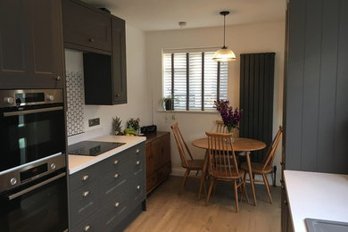 Inspiration for a small classic galley kitchen/diner in Sussex with a built-in sink, shaker cabinets, grey cabinets, laminate countertops, white splashback, ceramic splashback, integrated appliances, vinyl flooring, no island, brown floors and white worktops.