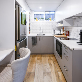 Photo of a small contemporary u-shaped eat-in kitchen in Sydney with a single-bowl sink, flat-panel cabinets, grey cabinets, quartz benchtops, white splashback, subway tile splashback, stainless steel appliances, ceramic floors, no island, brown floor and white benchtop.