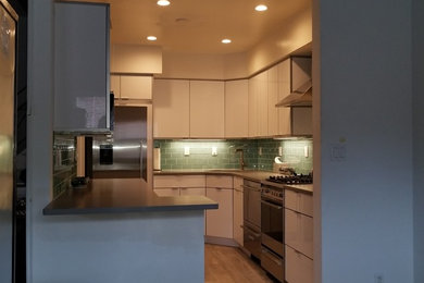 Mid-sized minimalist u-shaped porcelain tile and brown floor enclosed kitchen photo in New York with an undermount sink, flat-panel cabinets, white cabinets, quartz countertops, green backsplash, subway tile backsplash, stainless steel appliances, a peninsula and gray countertops