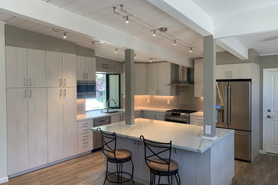 Mid-sized minimalist l-shaped laminate floor and multicolored floor eat-in kitchen photo in San Francisco with a single-bowl sink, flat-panel cabinets, light wood cabinets, solid surface countertops, beige backsplash, glass tile backsplash, stainless steel appliances, an island and white countertops