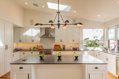 Medium sized rural u-shaped kitchen/diner in Los Angeles with a single-bowl sink, shaker cabinets, white cabinets, soapstone worktops, white splashback, metro tiled splashback, stainless steel appliances, light hardwood flooring, an island and black worktops.