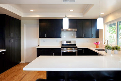 Mid-sized trendy u-shaped medium tone wood floor and brown floor eat-in kitchen photo in Los Angeles with a drop-in sink, shaker cabinets, dark wood cabinets, quartz countertops, white backsplash, stainless steel appliances, a peninsula and white countertops
