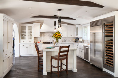 Photo of a large traditional u-shaped kitchen/diner in Santa Barbara with a belfast sink, recessed-panel cabinets, white cabinets, marble worktops, white splashback, metro tiled splashback, stainless steel appliances, dark hardwood flooring and an island.