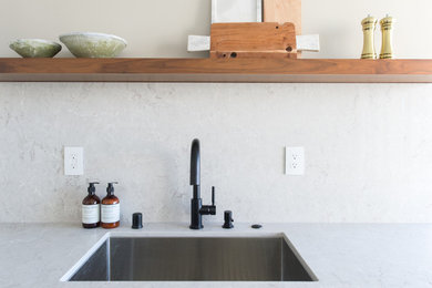 Exempel på ett mellanstort modernt kök, med en undermonterad diskho, skåp i shakerstil, vita skåp, bänkskiva i kvarts, vitt stänkskydd, stänkskydd i sten, rostfria vitvaror, klinkergolv i keramik, en köksö och grått golv