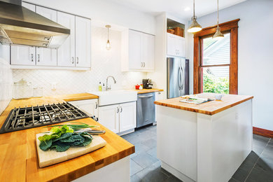 Classic l-shaped enclosed kitchen in Other with wood worktops, white splashback, stainless steel appliances and an island.