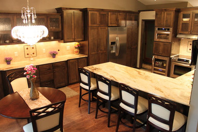 Example of a large classic l-shaped medium tone wood floor eat-in kitchen design in Minneapolis with recessed-panel cabinets, dark wood cabinets, marble countertops, beige backsplash, stainless steel appliances and a peninsula