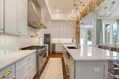 Photo of a large traditional u-shaped enclosed kitchen in New Orleans with a submerged sink, recessed-panel cabinets, grey cabinets, marble worktops, white splashback, stone slab splashback, stainless steel appliances, medium hardwood flooring, an island and brown floors.