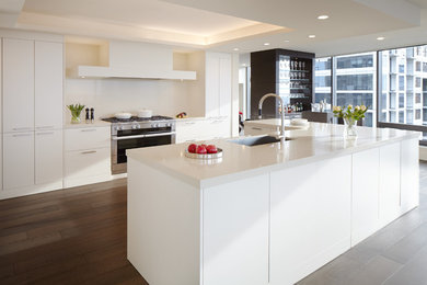 Example of a large minimalist l-shaped dark wood floor and brown floor open concept kitchen design in Seattle with quartz countertops, an undermount sink, flat-panel cabinets, white cabinets, white backsplash, stainless steel appliances, an island and white countertops