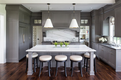 Example of a transitional u-shaped dark wood floor and brown floor eat-in kitchen design in Minneapolis with an undermount sink, recessed-panel cabinets, gray cabinets, white backsplash, stone slab backsplash, paneled appliances, an island and white countertops