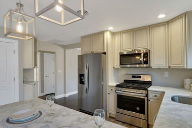 Inspiration for a mid-sized timeless u-shaped vinyl floor enclosed kitchen remodel in Philadelphia with an undermount sink, raised-panel cabinets, beige cabinets, marble countertops, white backsplash, porcelain backsplash, stainless steel appliances, a peninsula and white countertops
