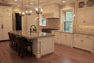 This is an example of an expansive traditional l-shaped open plan kitchen in Cincinnati with a double-bowl sink, raised-panel cabinets, white cabinets, granite worktops, beige splashback, stone tiled splashback, stainless steel appliances, medium hardwood flooring and an island.