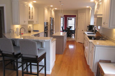 Example of a mid-sized classic galley light wood floor eat-in kitchen design in Providence with an undermount sink, raised-panel cabinets, white cabinets, quartz countertops, gray backsplash, stainless steel appliances and a peninsula