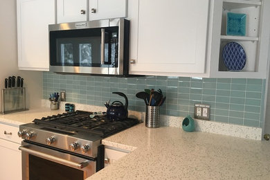Example of a classic l-shaped eat-in kitchen design in Providence with a double-bowl sink, recycled glass countertops, green backsplash, glass tile backsplash, stainless steel appliances and a peninsula