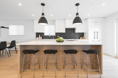 Trendy galley light wood floor and yellow floor open concept kitchen photo in Vancouver with an undermount sink, shaker cabinets, white cabinets, quartzite countertops, black backsplash, ceramic backsplash, paneled appliances, an island and multicolored countertops