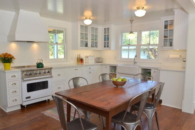 Small cottage u-shaped medium tone wood floor eat-in kitchen photo in Other with a farmhouse sink, beaded inset cabinets, white cabinets, quartz countertops, white backsplash, white appliances and no island