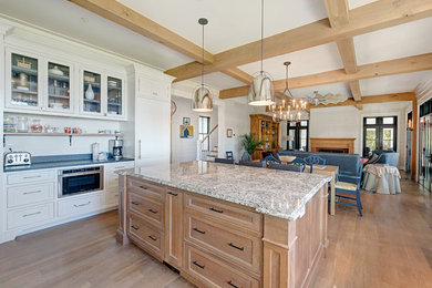 Example of a large farmhouse u-shaped medium tone wood floor and brown floor kitchen design in Baltimore with a farmhouse sink, shaker cabinets, white cabinets, granite countertops, mosaic tile backsplash, paneled appliances and an island