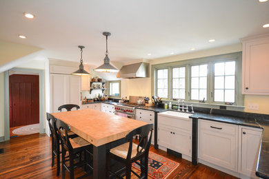 Mid-sized country u-shaped medium tone wood floor enclosed kitchen photo in New York with a farmhouse sink, shaker cabinets, white cabinets, marble countertops, black backsplash, stone slab backsplash, stainless steel appliances and an island
