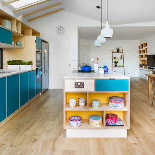 Scandinavian open plan kitchen in London with a submerged sink, flat-panel cabinets, turquoise cabinets, window splashback, light hardwood flooring, an island, beige floors and white worktops.