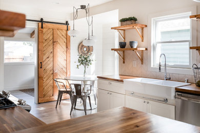 Example of a small country u-shaped laminate floor and gray floor kitchen design in Sacramento with a farmhouse sink, shaker cabinets, white cabinets, wood countertops, stainless steel appliances, white backsplash, subway tile backsplash and brown countertops