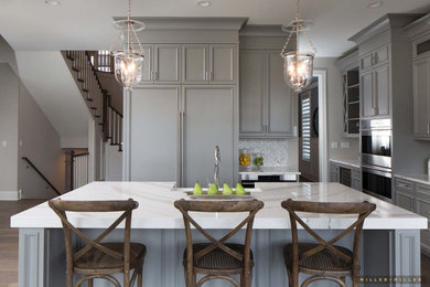 Example of a mid-sized cottage l-shaped medium tone wood floor and brown floor eat-in kitchen design in Chicago with a farmhouse sink, beaded inset cabinets, gray cabinets, marble countertops, gray backsplash, marble backsplash, paneled appliances, an island and white countertops