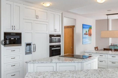 Foto på ett stort funkis kök, med en rustik diskho, luckor med infälld panel, vita skåp, bänkskiva i glas, grått stänkskydd, stänkskydd i stenkakel, integrerade vitvaror, mellanmörkt trägolv och en köksö
