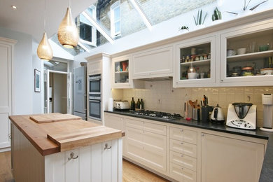 Photo of a medium sized classic single-wall kitchen in London with recessed-panel cabinets, white cabinets, wood worktops, light hardwood flooring, an island and brown floors.
