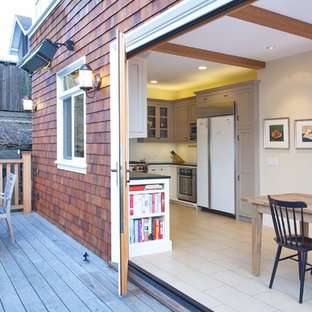 This is an example of a mid-sized arts and crafts u-shaped eat-in kitchen in San Francisco with white splashback, subway tile splashback, a farmhouse sink, beaded inset cabinets, white cabinets, solid surface benchtops, stainless steel appliances, ceramic floors, beige floor and black benchtop.