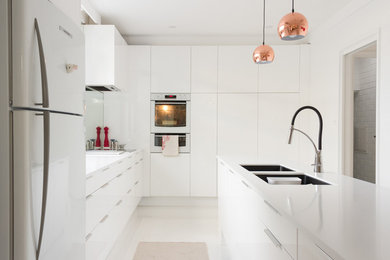 Foto på ett funkis kök, med en undermonterad diskho, släta luckor, vita skåp, granitbänkskiva, spegel som stänkskydd, vita vitvaror, klinkergolv i porslin och en köksö