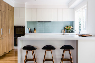 Пример оригинального дизайна: кухня среднего размера в стиле модернизм с кладовкой, светлыми деревянными фасадами, синим фартуком, фартуком из стеклянной плитки, черной техникой и коричневым полом