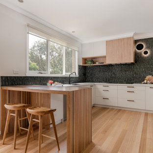 Inspiration for a contemporary u-shaped kitchen in Melbourne with an undermount sink, flat-panel cabinets, white cabinets, black splashback, panelled appliances, light hardwood floors, a peninsula, beige floor and white benchtop.