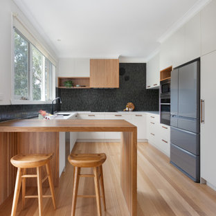 Photo of a contemporary u-shaped kitchen in Melbourne with an undermount sink, flat-panel cabinets, grey cabinets, black splashback, mosaic tile splashback, stainless steel appliances, light hardwood floors, a peninsula, beige floor and white benchtop.