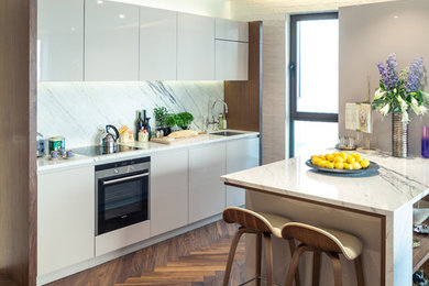 Moderne Küche mit Unterbauwaschbecken, flächenbündigen Schrankfronten, weißen Schränken, Küchenrückwand in Weiß, Küchengeräten aus Edelstahl, braunem Holzboden und Halbinsel in London