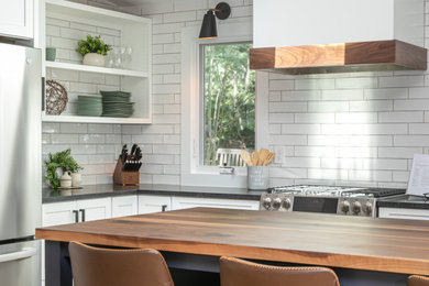 Example of a large eclectic l-shaped medium tone wood floor, brown floor and vaulted ceiling eat-in kitchen design in Raleigh with an undermount sink, shaker cabinets, white cabinets, wood countertops, white backsplash, porcelain backsplash, stainless steel appliances, an island and black countertops
