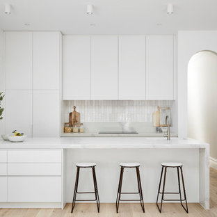 This is an example of a modern galley kitchen in Melbourne with an undermount sink, flat-panel cabinets, white cabinets, white splashback, panelled appliances, medium hardwood floors, a peninsula, brown floor and white benchtop.