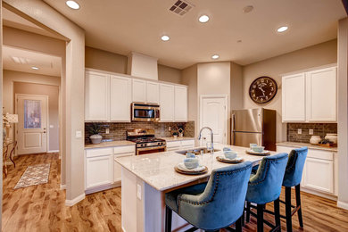Inspiration for a mid-sized transitional l-shaped light wood floor open concept kitchen remodel in Las Vegas with an undermount sink, recessed-panel cabinets, white cabinets, granite countertops, gray backsplash, glass tile backsplash, stainless steel appliances and an island