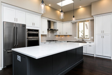 Example of a large transitional l-shaped dark wood floor and brown floor eat-in kitchen design in Albuquerque with a farmhouse sink, shaker cabinets, white cabinets, quartz countertops, gray backsplash, subway tile backsplash, stainless steel appliances and an island