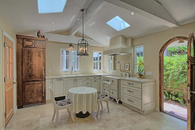 Example of a small classic l-shaped ceramic tile eat-in kitchen design in Orange County with a single-bowl sink, raised-panel cabinets, white cabinets, solid surface countertops, beige backsplash, stone slab backsplash, stainless steel appliances and an island