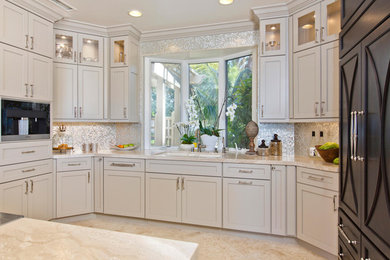 Example of a mid-sized transitional l-shaped travertine floor open concept kitchen design in San Diego with an undermount sink, recessed-panel cabinets, beige cabinets, limestone countertops, beige backsplash, glass tile backsplash, stainless steel appliances and an island