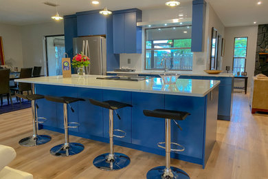 Example of a mid-sized trendy single-wall open concept kitchen design with flat-panel cabinets, blue cabinets, quartz countertops, white backsplash, an island and white countertops