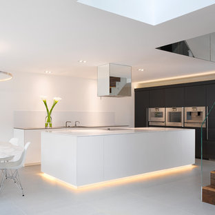 This is an example of a contemporary open plan kitchen in London with flat-panel cabinets, black cabinets, white splashback, stainless steel appliances, an island, white floors and white worktops.