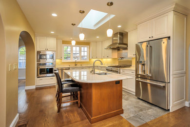 Example of a classic l-shaped open concept kitchen design in Other with an undermount sink, raised-panel cabinets, granite countertops, beige backsplash and stainless steel appliances
